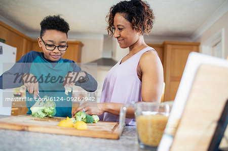 Mother and son cooking, cutting vegetables in kitchen