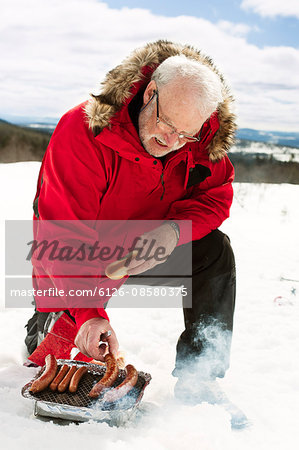 Sweden, Dalarna, idre, Man cooking hot-dogs in snow