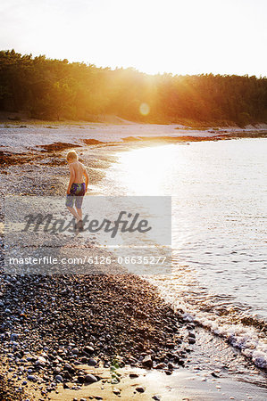 Sweden, Gotland, Lickershamn, Boy (8-9) walking on beach at sunset
