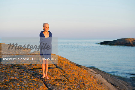 Sweden, Sodermanland, Stockholm Archipelago, Varmdo, Boy (12-13) wrapped in towel on rocky beach