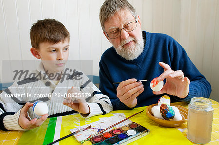 Grandfather with grandson (8-9) decorating Easter eggs
