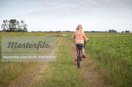 Sweden, Skane, Soderslatt, Beddinge, Blonde girl (10-11) riding bike along dirt road in green field