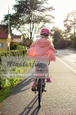 Sweden, Vastergotland, Lerum, Girl (10-11) wearing pink helmet riding bicycle along street