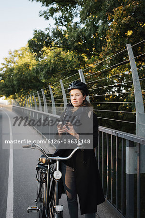 Sweden, Sodermanland, Stockholm, Vasterbron, Young woman standing by bicycle using phone