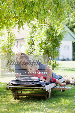 Sweden, Skane, Mossby, Daughter with father lying on deckchair and using tablet pc