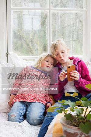 Sweden, Sisters (4-5, 10-11) using smart phone at home