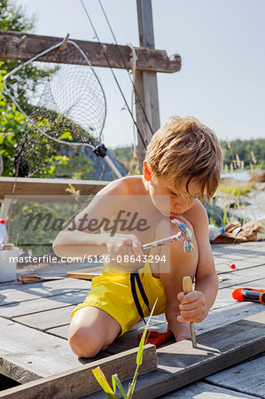 Sweden, Uppland, Runmaro, Barrskar, Boy (4-5) repairing wooden deck
