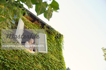 Italy, Tuscany, Dicomano, Woman looking out from window of overgrown house