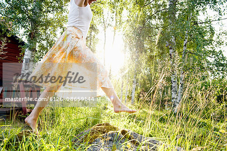 Sweden, Dalarna, Svardsjo, Young woman jumping in grass in backyard