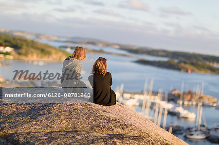 Sweden, Gotaland, Bohuslan, Grebbestad, Mid adult women sitting on rock overlooking port and bay