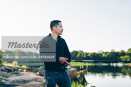 Sweden, Karlskrona, Blekinge, Man standing on lake shore and fishing