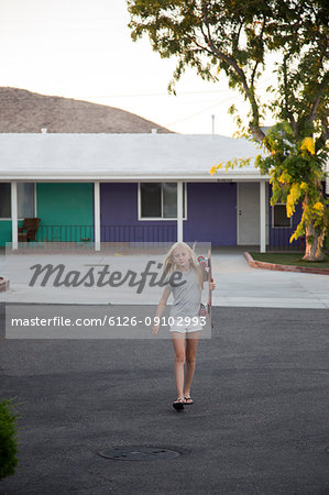 Girl carrying skateboard with motel in background