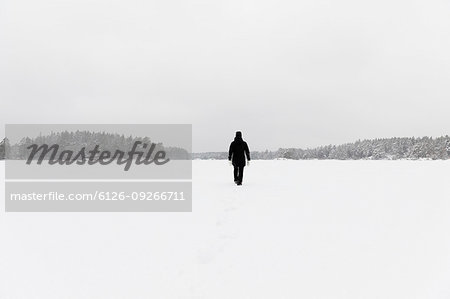 Woman wearing black walking on snow covered Stora Skiren lake in Lotorp, Sweden