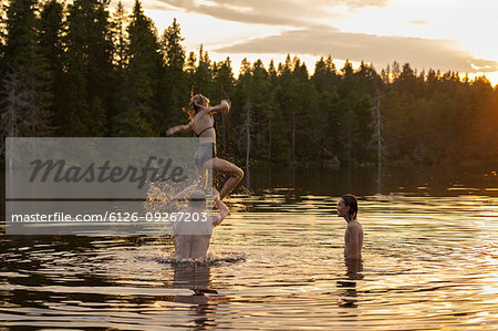 Man throwing teenage girl over lake at sunset