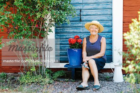 Senior woman sitting by flower pot in front of door