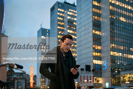 Young man holding cell phone walking down city street