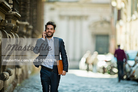 Cheerful young businessman makes a call as he is running along the street late for work.