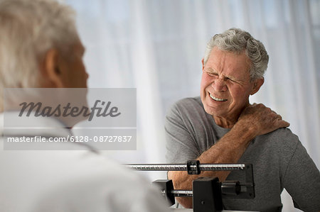 Mature man grips his shoulder in pain while attending a medical examination.