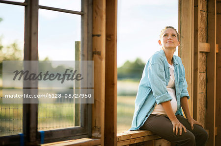 Expectant mother sitting in the window frame of a home under construction.