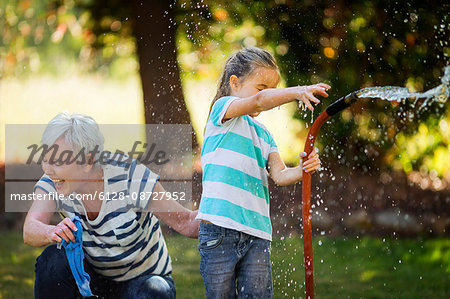 Happy grandmother and granddaughter spraying a hose on a summer day.