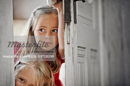 Two young girls peering around a doorframe.