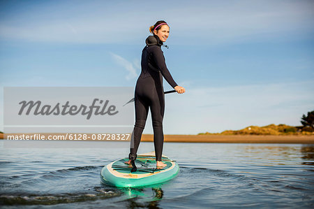 Smiling young woman paddleboarding on a lake. Stock Photo
