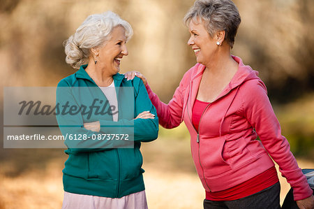 Two smiling senior woman doing stretching exercises together in a park.