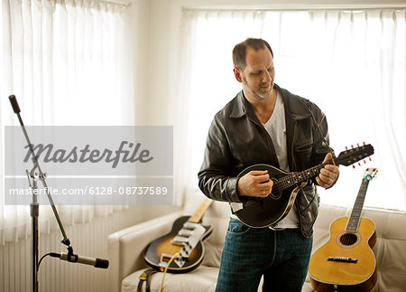 Mid-adult man playing a guitar in his living room.