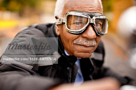 Portrait of a senior man sitting on a motorcycle wearing riding goggles.