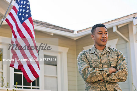 Young adult soldier standing with his arms crossed outside his home.