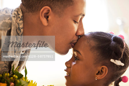 Soldier kissing his young daughter on the forehead.