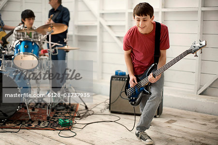 Teenage boy playing a bass guitar enthusiastically.