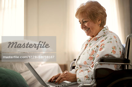 Smiling senior woman having fun using a laptop while sitting in a wheelchair.