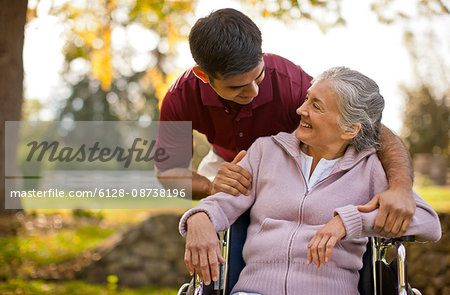 Smiling senior woman being comforted by a male nurse while sitting in a wheelchair inside a park.
