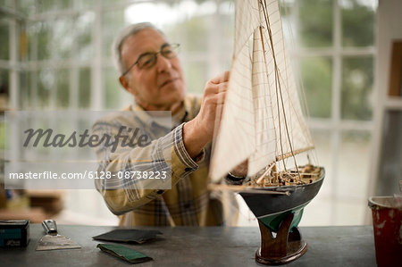 Senior man working on a model boat inside his garage.