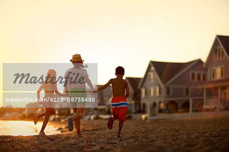 Mother and her two children holding hands and running on the beach at sunset.