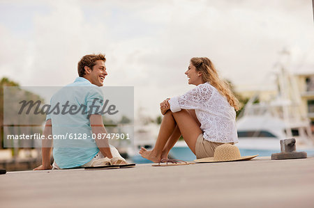 Smiling young couple sitting together on a jetty.