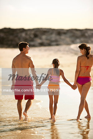 Family walking and holding hands on a beach.