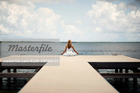 Relaxed middle-aged woman meditating while sitting on the end of a wooden jetty.