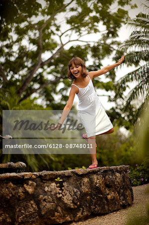 Smiling young girl having fun balancing on the stone wall of a garden fishpond.