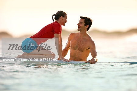 Mid-adult woman facing her boyfriend as she learns how to surf.