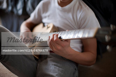 Boy sitting on bed playing guitar.