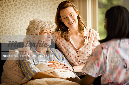 Young woman sits on the edge of a bed and puts a reassuring arm around a senior woman.