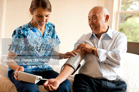 Senior man having his blood pressure checked by a nurse at home.