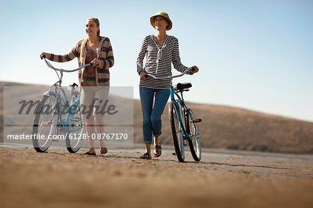 Mother and daughter walking their bikes on a beach.
