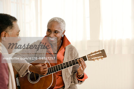 Happy senior man teaching his wife how to play guitar.