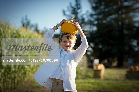 Portrait of a young boy carrying a pumpkin on his head.