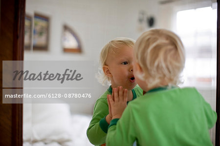 Young toddler in nappies looking at his reflection in a bedroom mirror.