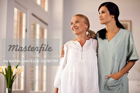 Female nurse standing with her arm around senior female patient as they look out window. Female nurse standing with her arm around senior female patient as they look out window.