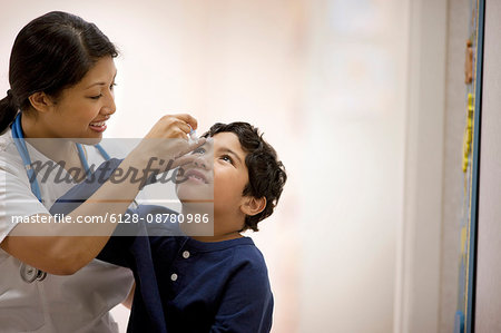 Nurse administering eye drops to a young boy.